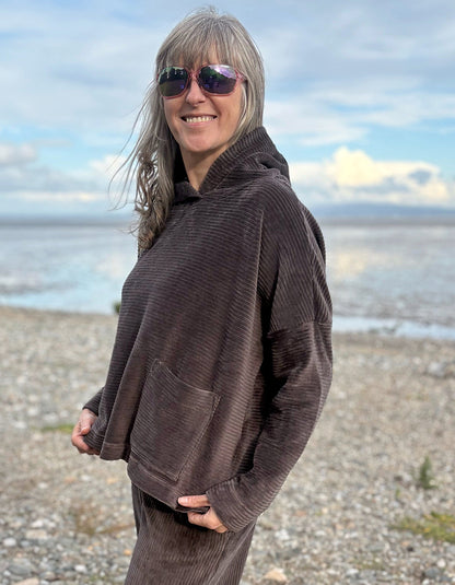 Person wearing a brown cord hooded sweater on a beach with ocean and sky in the background