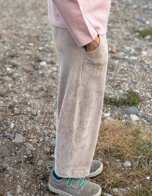 Person wearing light-colored corduroy pants and a pink sweater on a rocky ground.