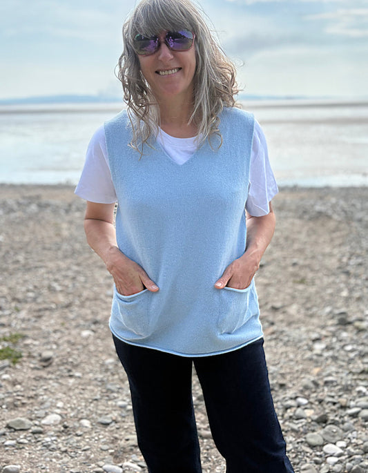 lady wearing a light blue sleeveless top and sunglasses on a beach. light blue wool sweater vest