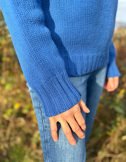 Person wearing a blue knitted sweater and jeans in an outdoor setting