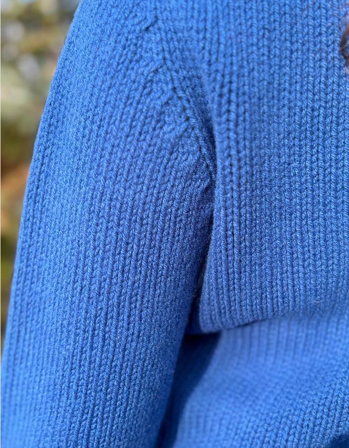 Close-up of a blue knitted sweater sleeve with a blurred natural background