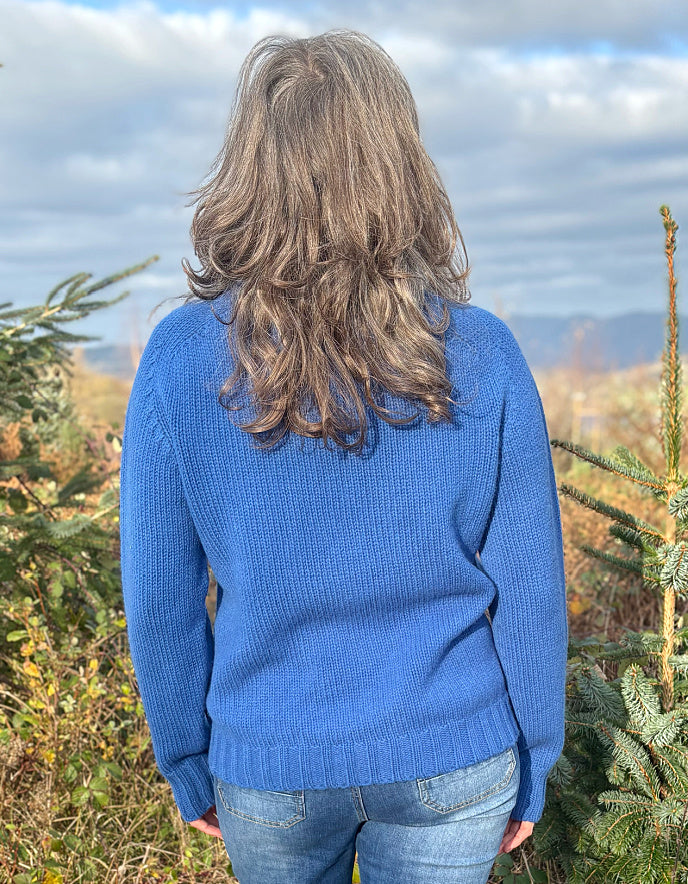 Person wearing a blue sweater standing among trees with a scenic background