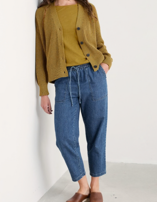 Person wearing a mustard yellow cardigan and blue jogger style jeans on a white background