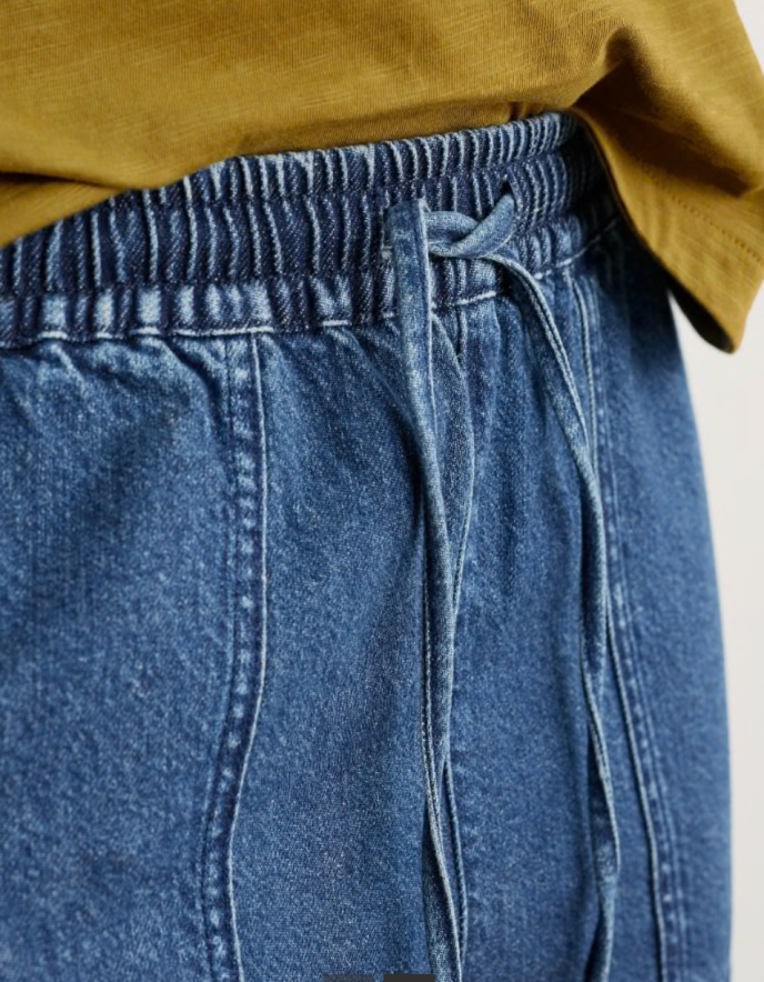 Person wearing a mustard yellow cardigan and blue jogger style jeans on a white background