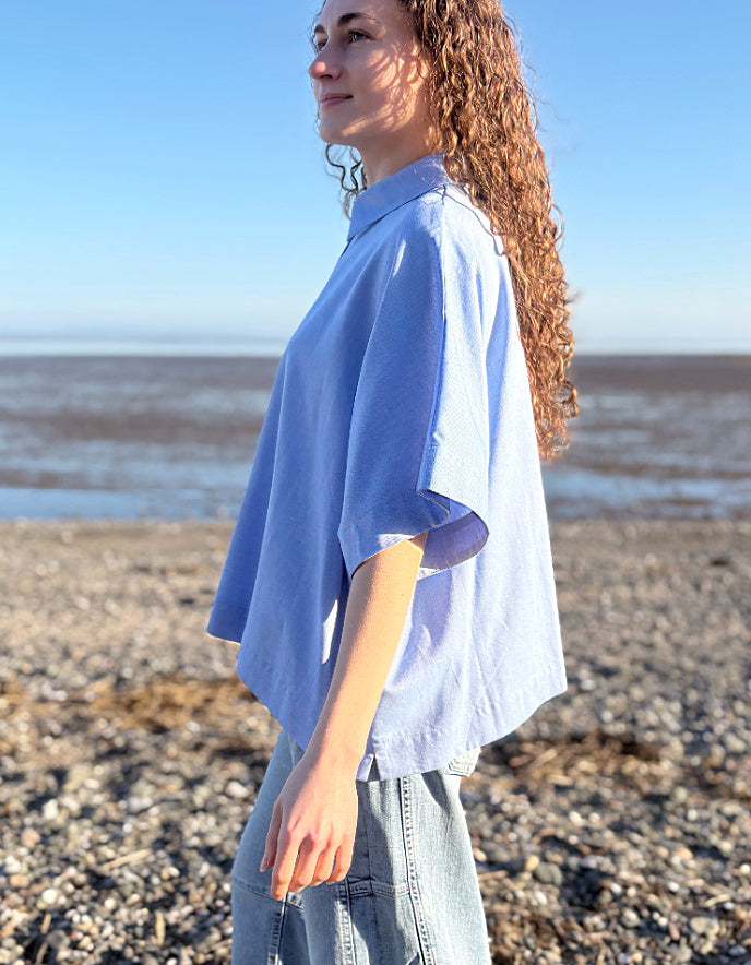 Woman wearing a light blue shirt and jeans standing on a beach.