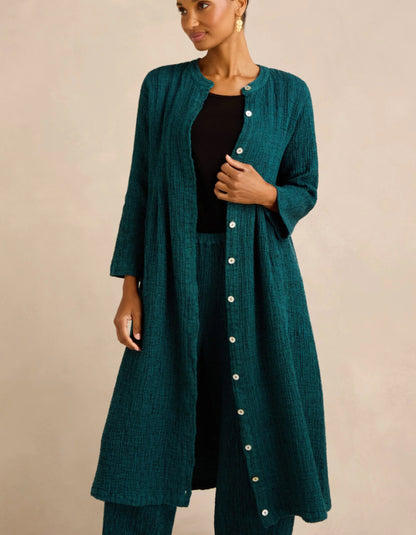 A woman models a long, dark teal-green textured button-up cardigan over a black outfit, set against a plain beige studio background.