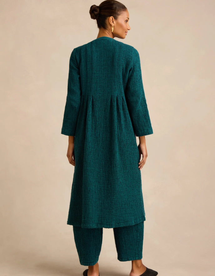 A woman shown from the back wearing a dark teal-green textured kurta and matching pants against a plain beige studio background.
