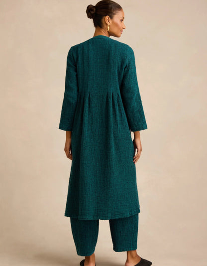 A woman shown from the back wearing a dark teal-green textured kurta and matching pants against a plain beige studio background.