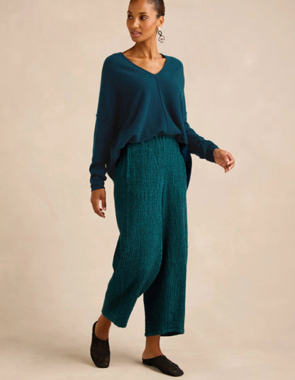 A woman modeling a dark teal long-sleeve knit top and matching textured teal wide-leg cropped pants against a plain beige studio background.