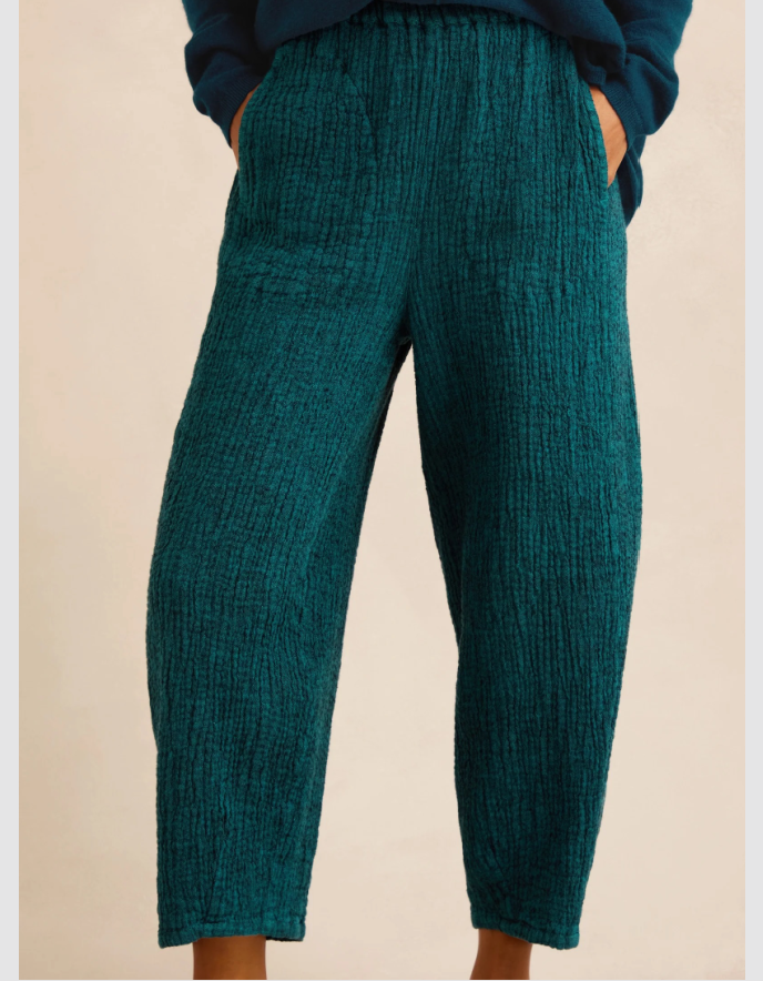 A person wearing textured teal cropped pants with a relaxed, slightly tapered leg and side pockets, paired with a dark blue top against a plain beige background.