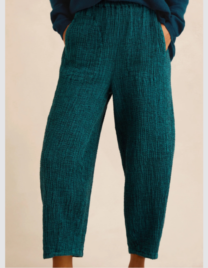 A person wearing textured teal cropped pants with a relaxed, slightly tapered leg and side pockets, paired with a dark blue top against a plain beige background.