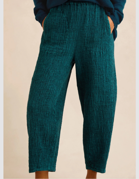 A person wearing textured teal cropped pants with a relaxed, slightly tapered leg and side pockets, paired with a dark blue top against a plain beige background.