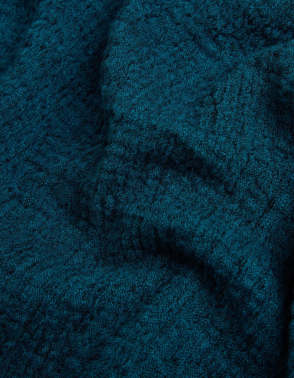 A close-up of a dark teal textured fabric, showing a detailed knit or woven pattern with soft folds and shadows.