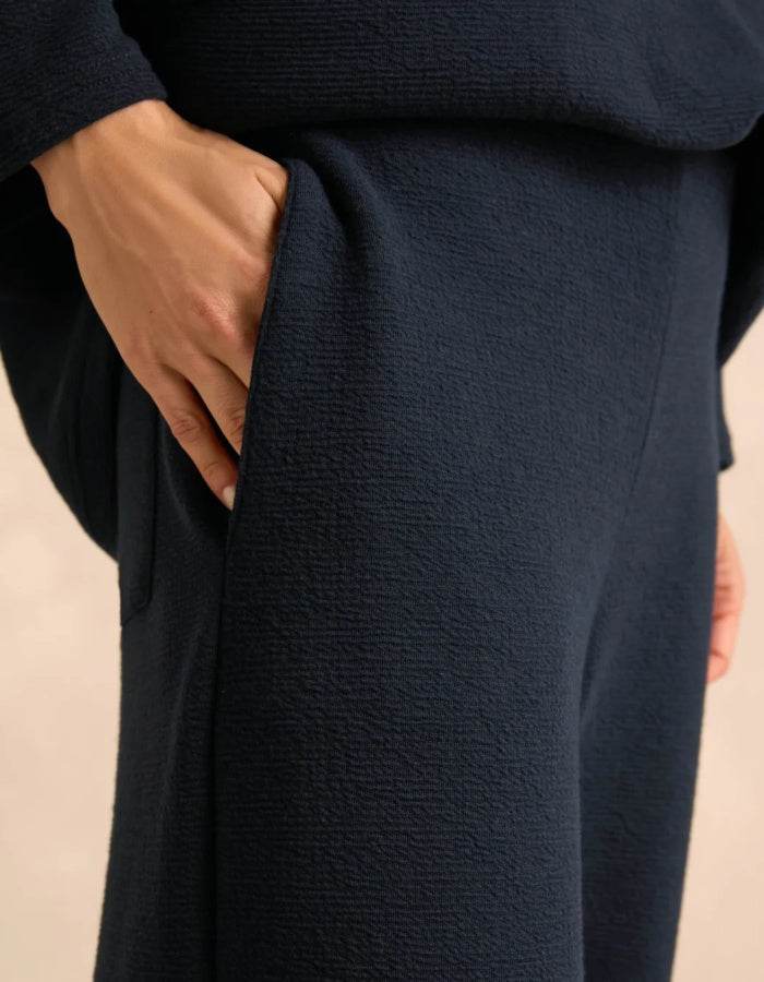 Close-up of a person wearing dark navy textured knit clothing, showing a hand tucked into a side pocket.