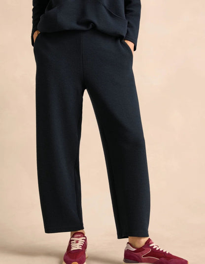 A person wearing dark navy wide-leg cropped pants with a matching dark top, paired with burgundy sneakers, standing against a plain beige studio background.