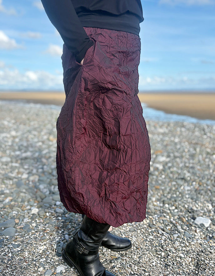 Person wearing a burgundy quilted skirt on a beach with a blue sky.