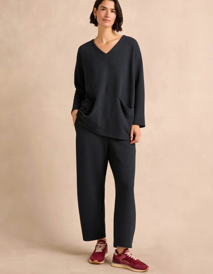 A woman wearing a navy V-neck long-sleeve tunic with side pockets, posed against a solid beige background.
