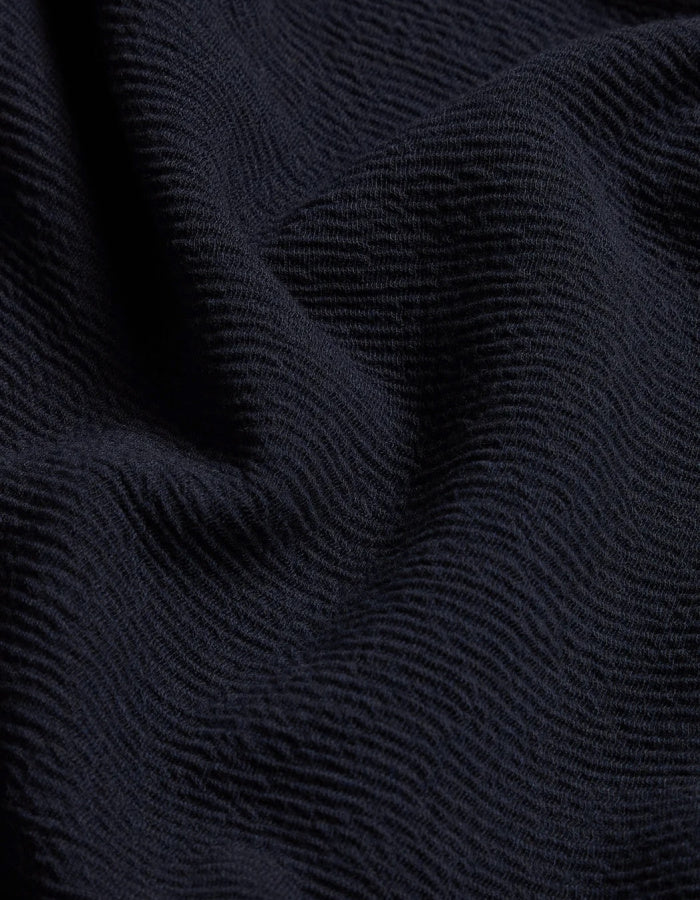 A close-up of dark navy blue textured fabric with a fine ribbed or wavy knit pattern and soft folds.