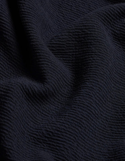 A close-up of dark navy blue textured fabric with a fine ribbed or wavy knit pattern and soft folds.