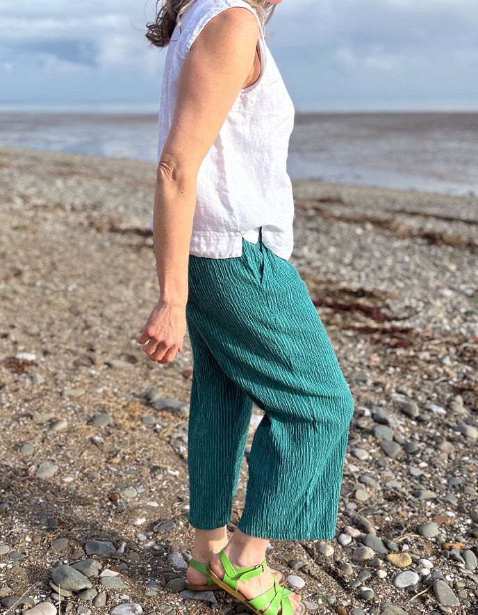 woman wearing teal cropped trouser and white linen top 