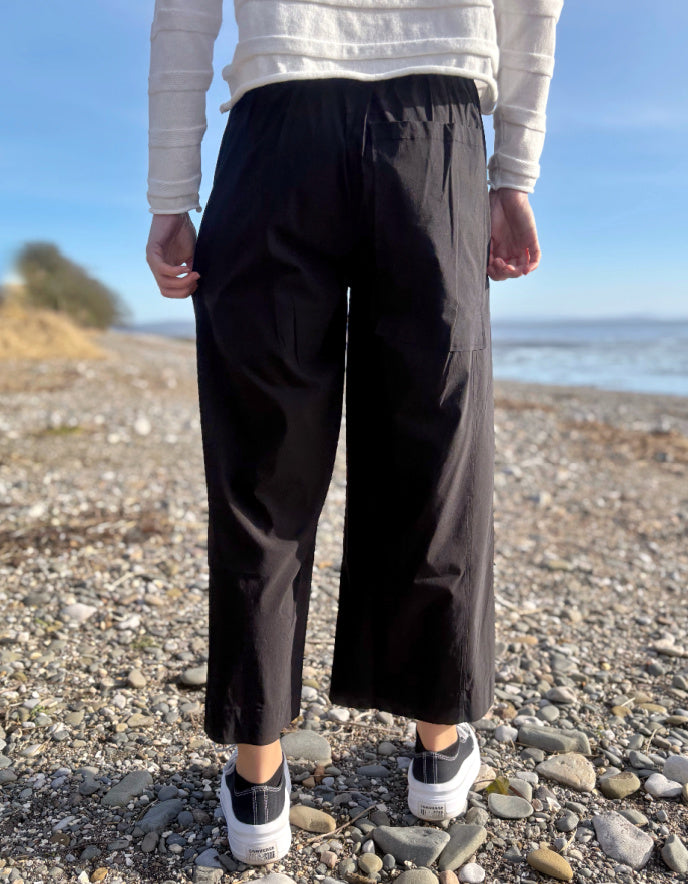 Person wearing black pants and a white sweater standing on a pebbly beach.