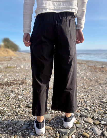 Person wearing black pants and a white sweater standing on a pebbly beach.