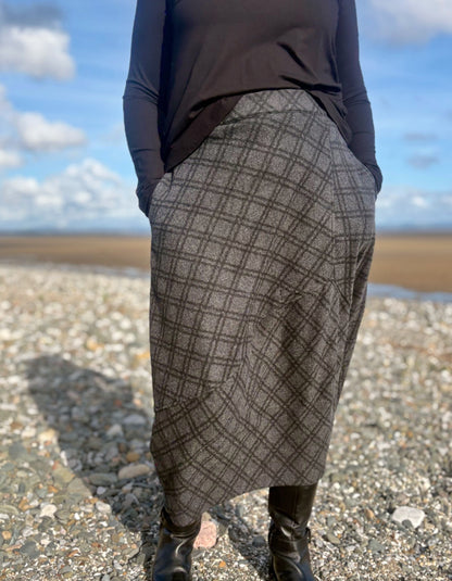 Person wearing a patterned skirt standing on a beach with a blue sky.