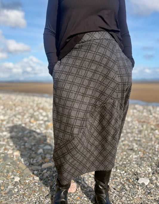 Person wearing a patterned skirt standing on a beach with a blue sky.