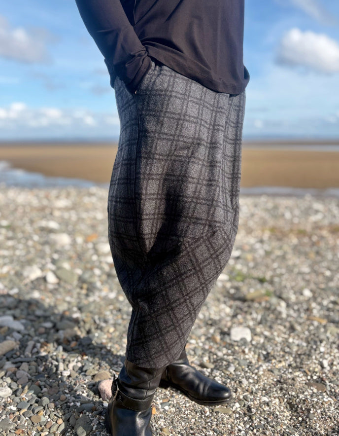 Person wearing checkered pants standing on a beach with a blue sky and clouds in the background.