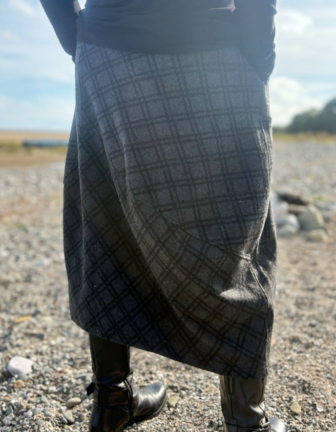 Person wearing a plaid skirt outdoors on a gravelly surface with a blurred background