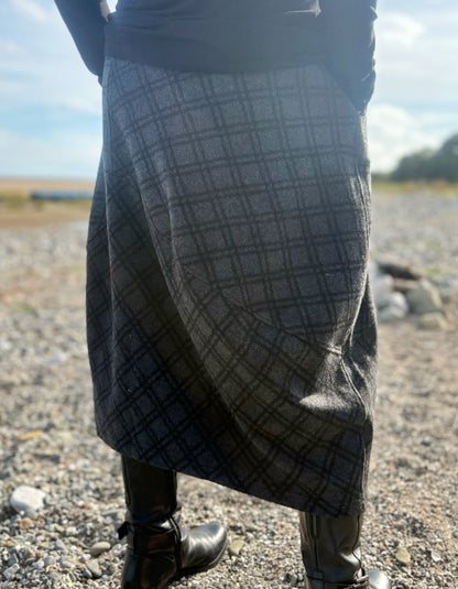 Person wearing a plaid skirt outdoors on a gravelly surface with a blurred background