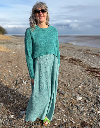 Woman in teal outfit standing on a beach with ocean and sky in the background