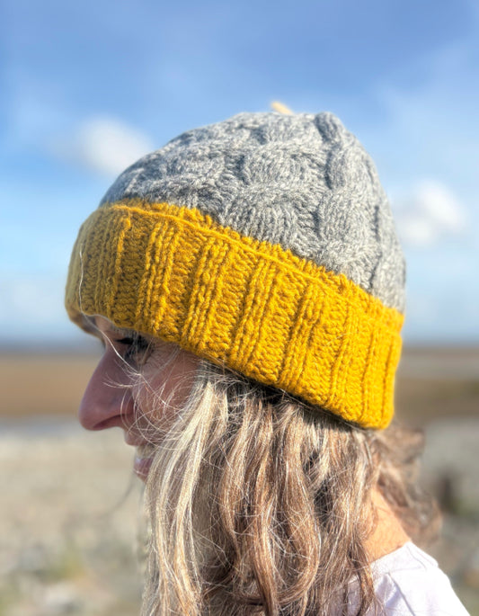 Person wearing a gray and yellow knit beanie outdoors with a blurred natural background