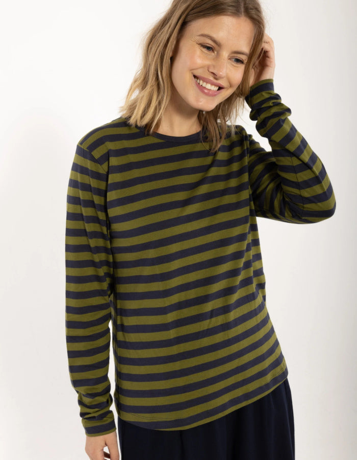 A woman wearing a long-sleeve striped top with olive green and dark navy horizontal stripes, paired with dark navy pants, against a plain white studio background.