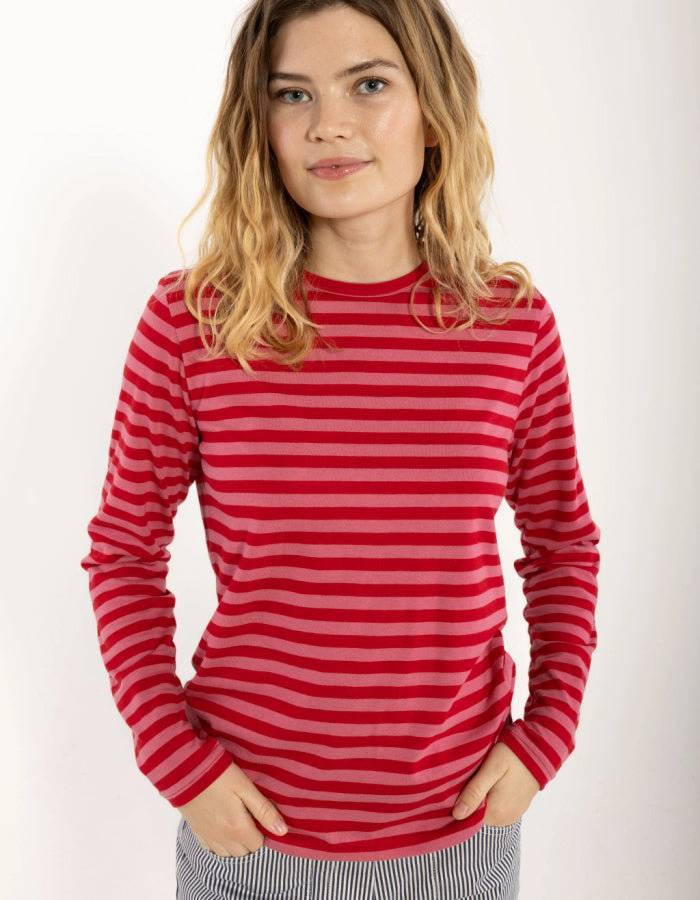 A woman wearing a red and pink striped long-sleeve crewneck top, standing against a plain white background.