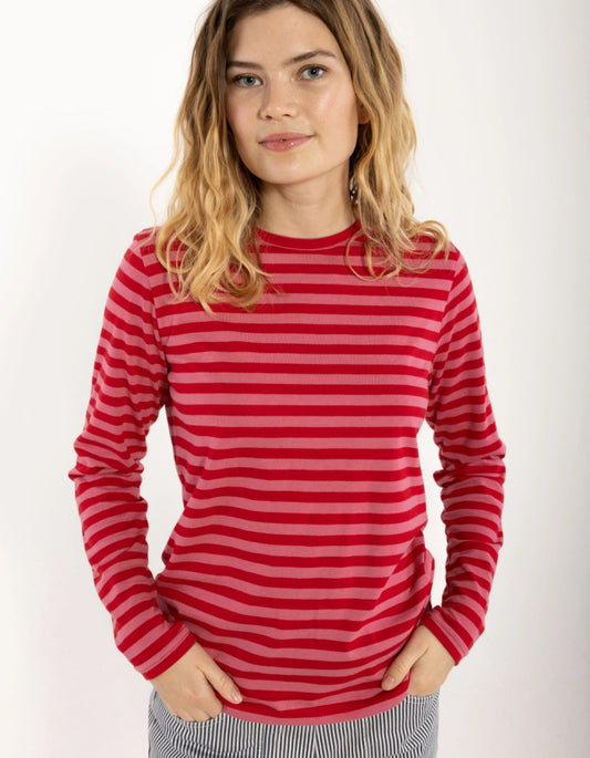 A woman wearing a red and pink striped long-sleeve crewneck top, standing against a plain white background.