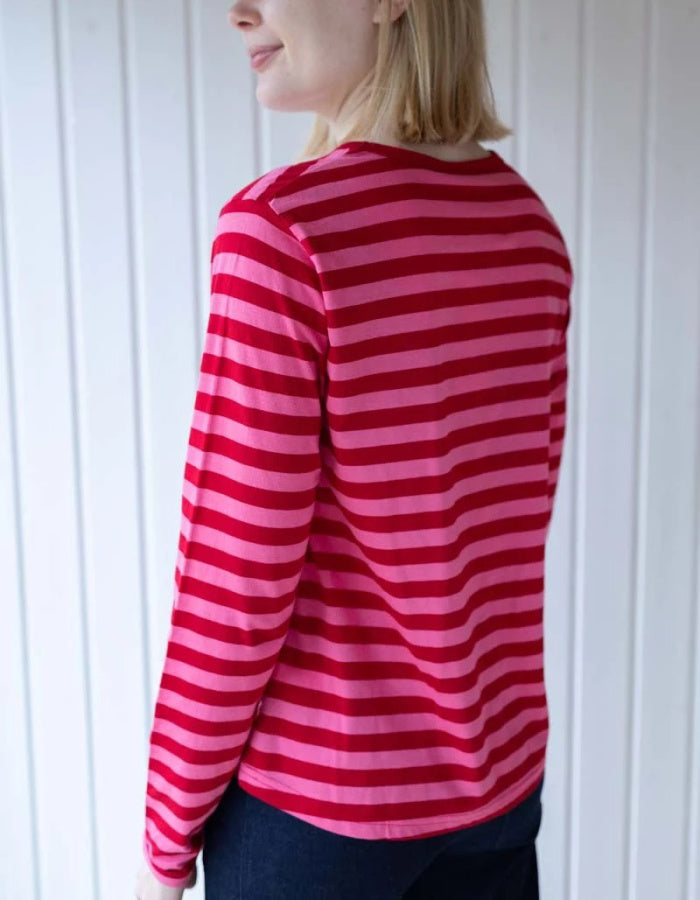 A woman wearing a pink and red striped long-sleeve top, shown from a side-back angle against a white paneled wall.