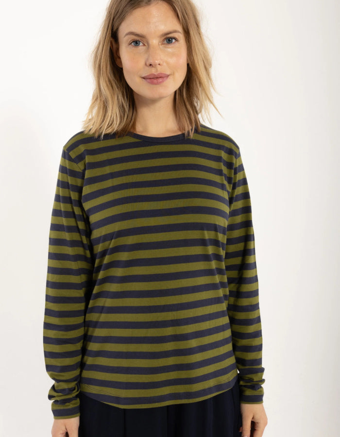 A woman wearing a long-sleeve crewneck top with horizontal olive green and dark navy stripes, photographed against a plain white studio background.