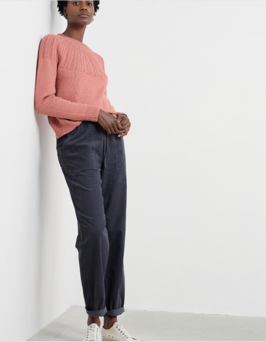 Person wearing a pink sweater and dark corduroy pants against a white background