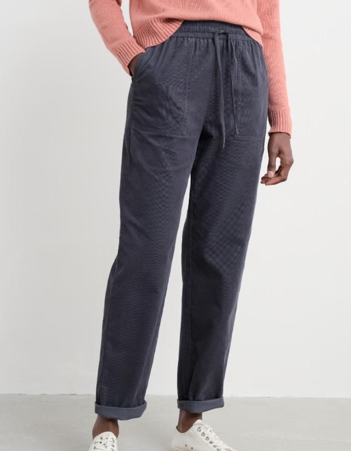 Person wearing a pink sweater and dark corduroy pants against a white background
