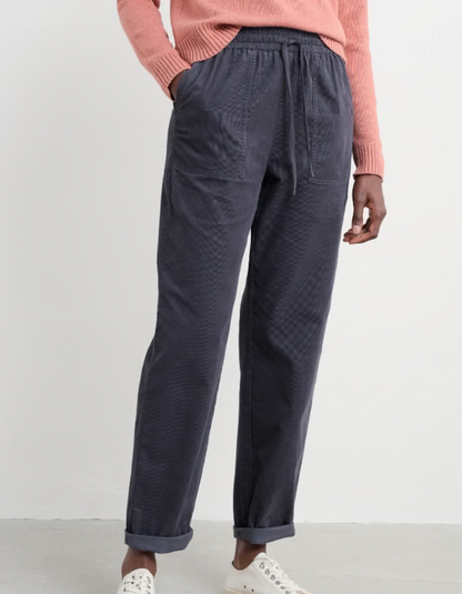 Person wearing a pink sweater and dark corduroy pants against a white background