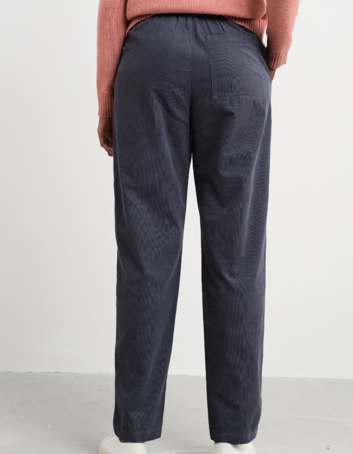 Person wearing a pink sweater and dark grey corduroy pants against a white background