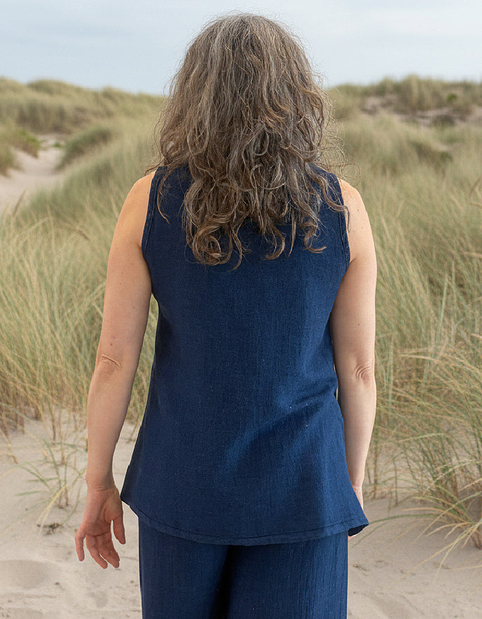Person wearing a blue sleeveless top and pants standing in sand dunes