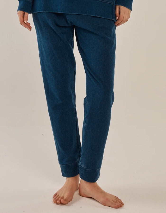 A person wearing dark blue cropped pants and a matching top, shown from the waist down against a plain light beige studio background.