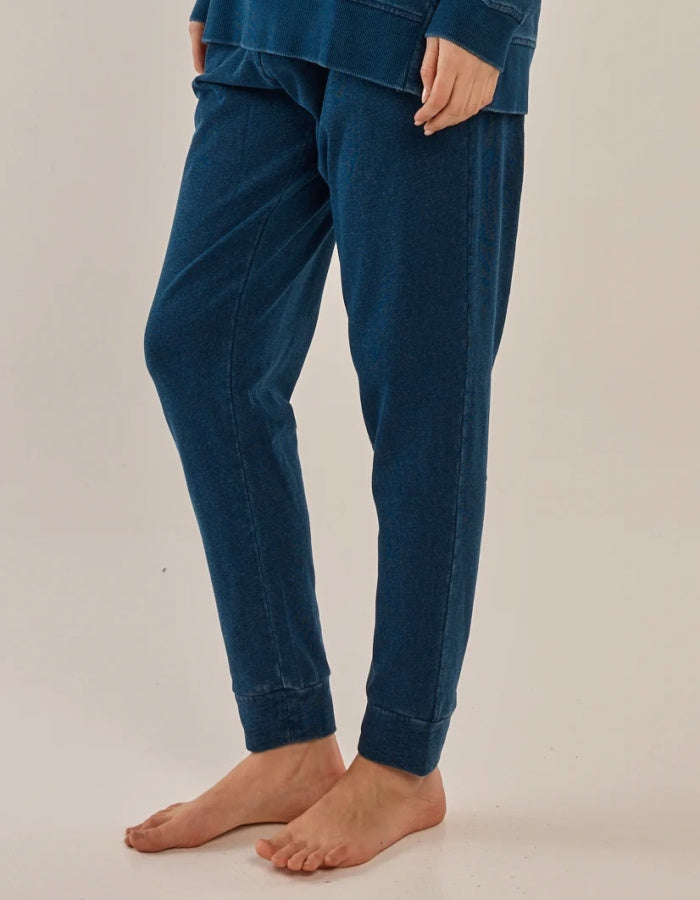 A person wearing dark blue jogger-style pants with a relaxed fit and cuffed ankles, shown from the waist down against a plain light beige studio background.