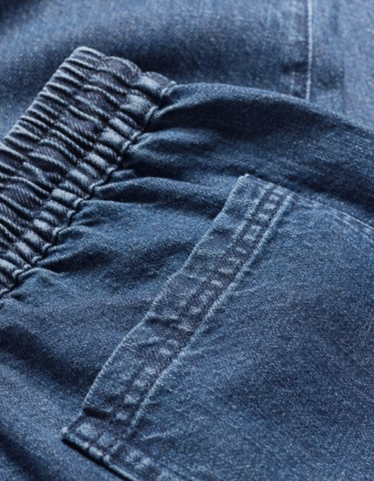 Person wearing a mustard yellow cardigan and blue jogger style jeans on a white background