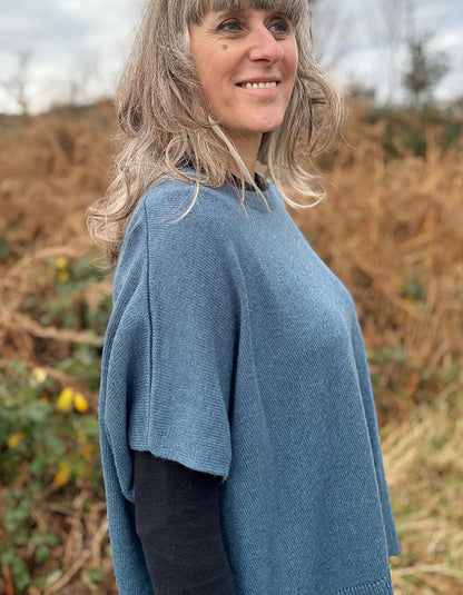 Woman wearing a blue sweater standing in a field with dry grass and trees in the background