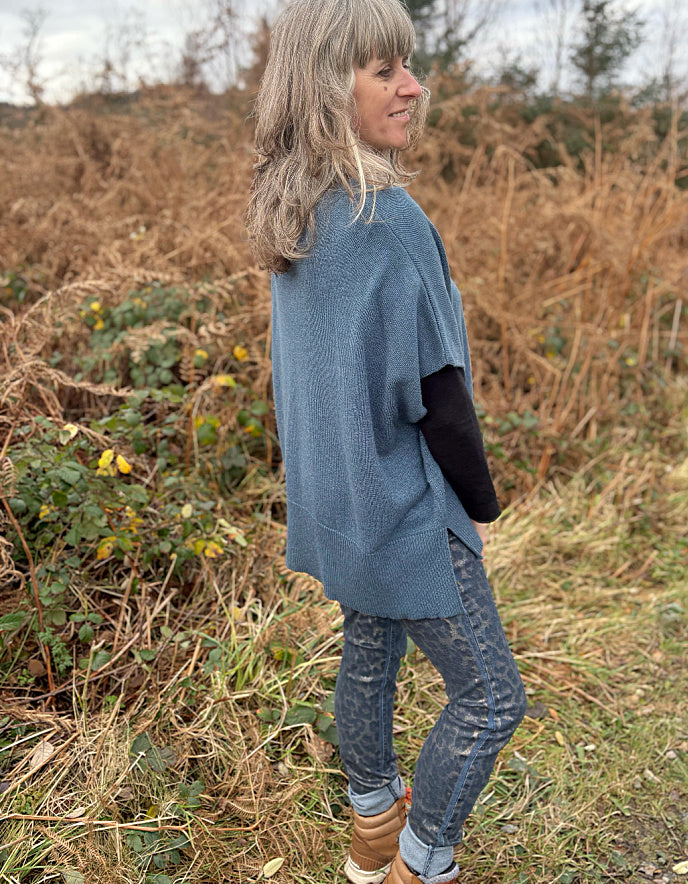 Person wearing a blue poncho standing in a field with dry grass and plants.
