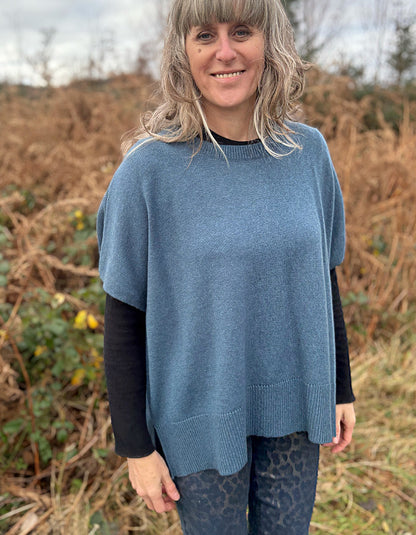 Person wearing a blue poncho standing in a natural setting with dry grass and trees.