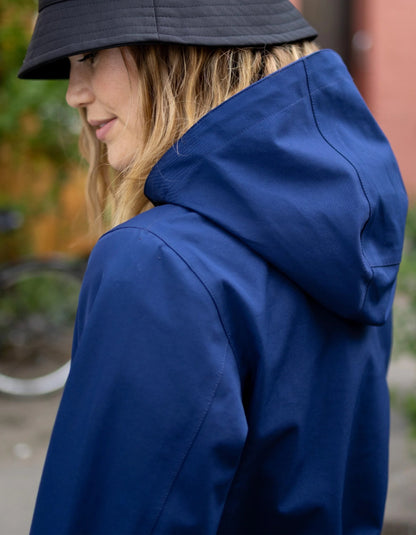 A woman wearing a navy blue hooded jacket and a dark bucket hat, shown in a side profile view against an outdoor blurred background.